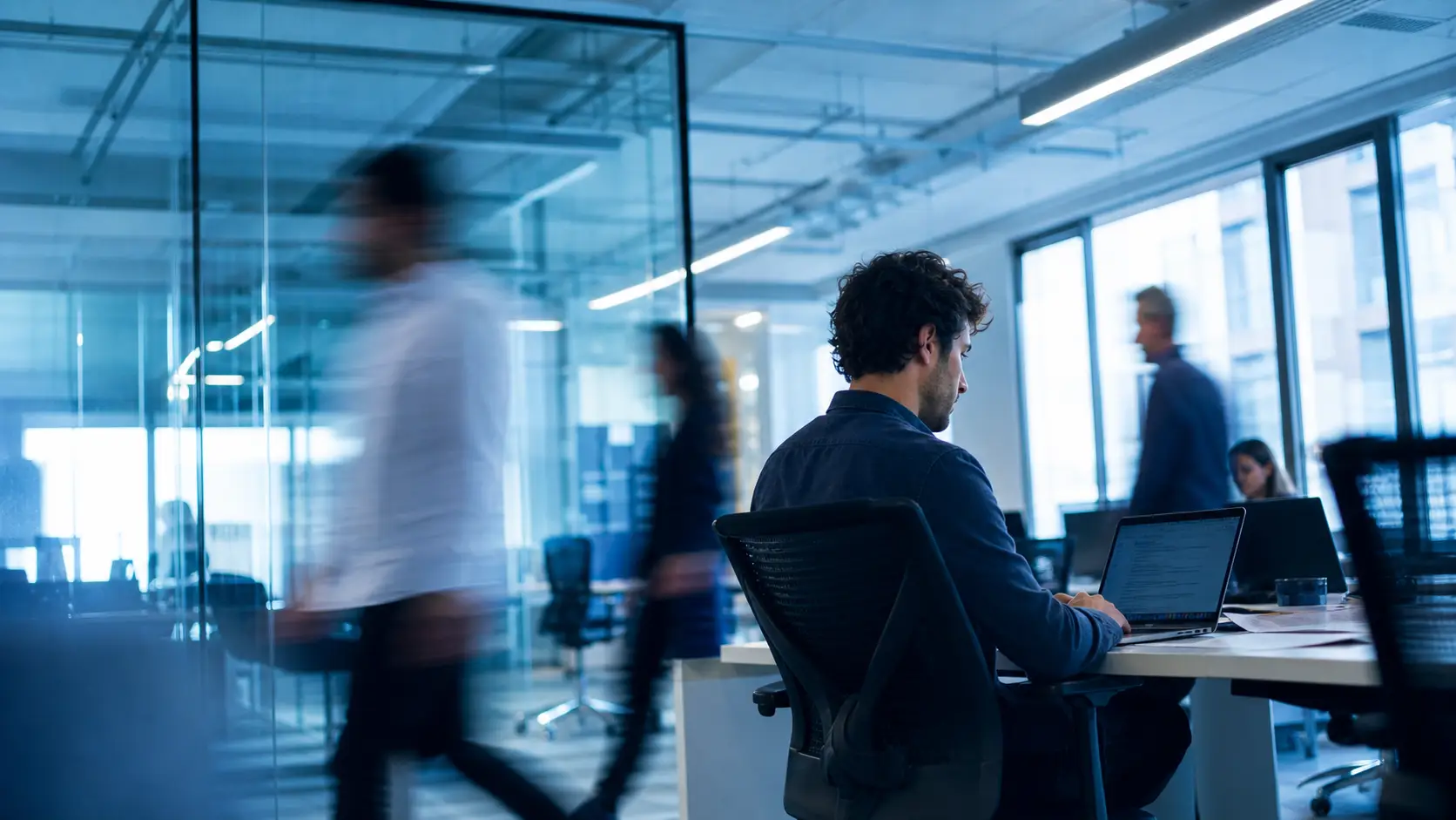Profesional trabajando mientras el equipo se mueve alrededor en una oficina abierta